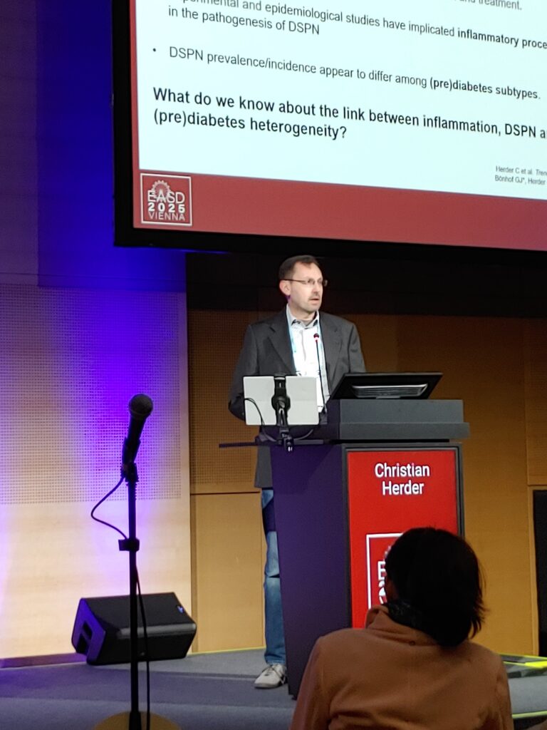 Professor Christian Herder from Düsseldorf (Germany) stands behind the lectern on the stage and gives his presentation.